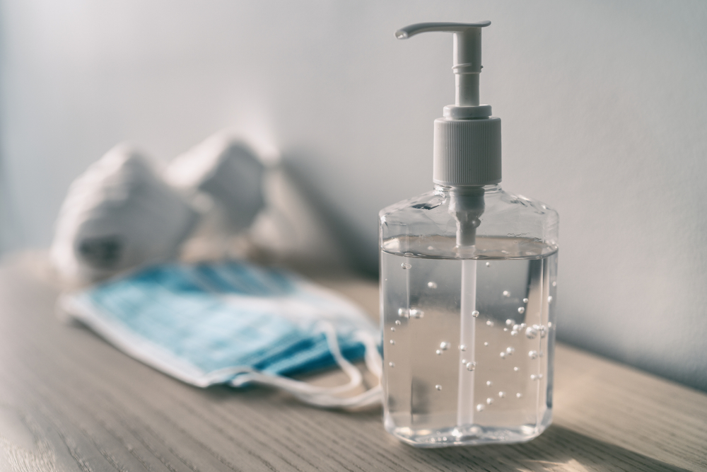 Clear bottle of diluted rubbing alcohol with a pump dispenser, alongside medical masks on a wooden surface, used as a disinfectant to treat surfaces against bed bugs.